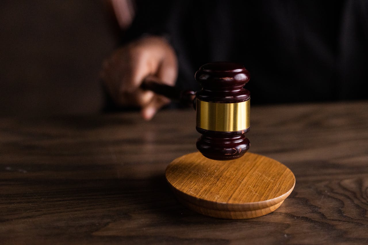 A wooden gavel with a gold band is poised above a circular wooden base on a table.